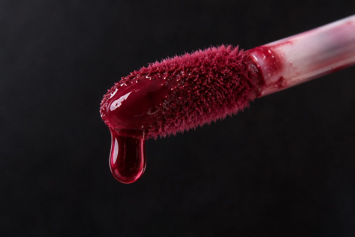 Flocked lip tint applicator with droplet of berry stain.